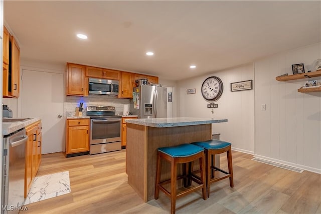 7080 Wren Ave NW, North Canton, OH 44720 - kitchen with stainless steel appliances, light wood-style flooring, a center island, a kitchen breakfast bar, and decorative backsplash
