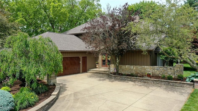 2307 Deerpath Dr, Sandusky, OH 44870 - view of property hidden behind natural elements with roof with shingles, a garage, stone siding, driveway, and board and batten siding