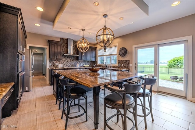 854 Crosstree Ln, Sandusky, OH 44870 - kitchen featuring wall chimney exhaust hood, a chandelier, backsplash, a kitchen bar, and dark brown cabinetry
