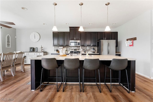 2979 Cloverhurst St NE, Canton, OH 44721 - kitchen featuring stainless steel appliances, light countertops, a large island with sink, decorative backsplash, and light wood-style flooring