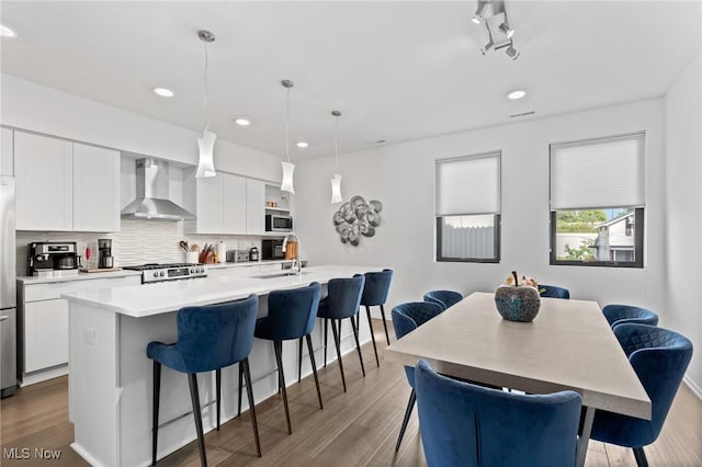 2317 Scranton Rd, Cleveland, OH 44113 - kitchen featuring wall chimney range hood, a kitchen breakfast bar, an island with sink, appliances with stainless steel finishes, and white cabinetry