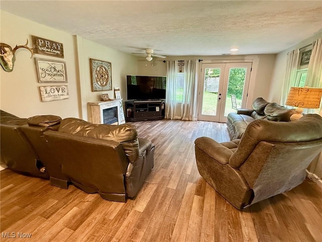 1550 Swift Rd, Waterford, OH 45786 - living room featuring a textured ceiling, light wood finished floors, french doors, ceiling fan, and a glass covered fireplace