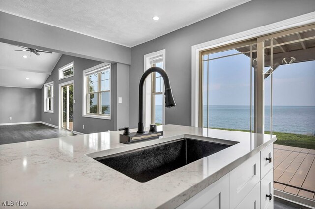 7569 Lake Shore Blvd, Madison, OH 44057 - kitchen with light stone countertops, dark wood-style floors, white cabinets, a water view, and ceiling fan