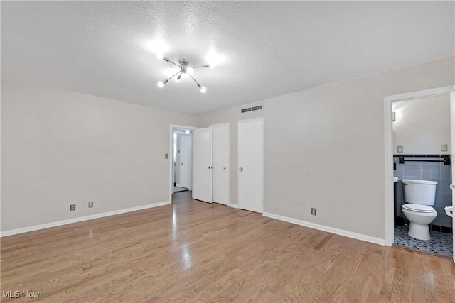 15875 Van Aken Blvd Unit 101C, Shaker Heights, OH 44120 - unfurnished bedroom featuring light wood-style flooring, ensuite bath, and a textured ceiling