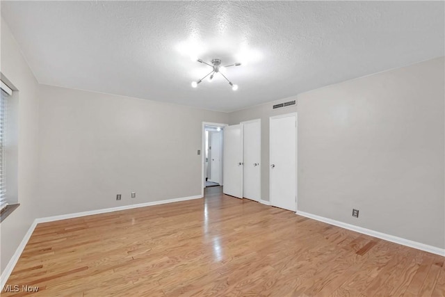15875 Van Aken Blvd Unit 101C, Shaker Heights, OH 44120 - unfurnished bedroom featuring light wood-type flooring, a textured ceiling, and a chandelier