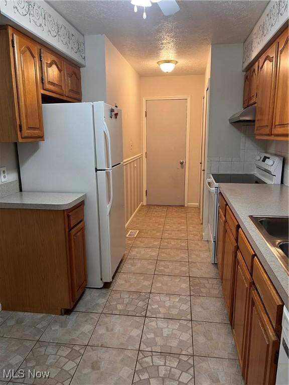 1235 Canyon View Rd, Sagamore Hills, OH 44067 - kitchen with electric stove, freestanding refrigerator, brown cabinets, a textured ceiling, and under cabinet range hood