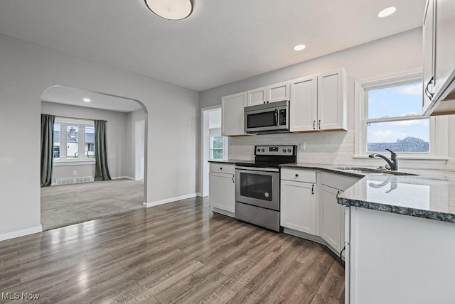 2515 Saratoga Ave SW, Canton, OH 44706 - kitchen with stainless steel appliances, dark stone counters, dark wood-style floors, white cabinets, and arched walkways