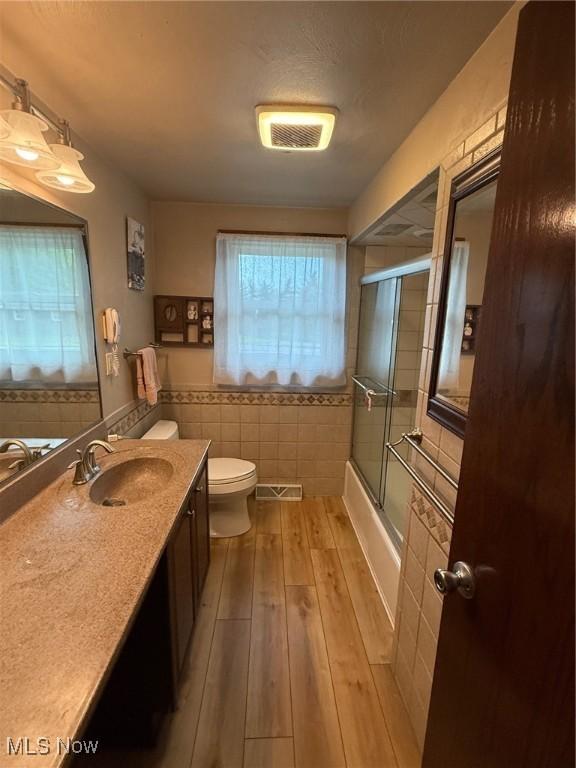 213 Highland Park, Bloomingdale, OH 43910 - full bathroom featuring wood finished floors, vanity, shower / bath combination with glass door, and tile walls