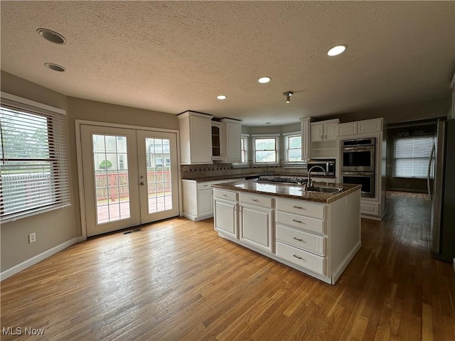 5330 Willow Ln, Sheffield Lake, OH 44054 - kitchen with appliances with stainless steel finishes, a textured ceiling, light wood-style floors, a kitchen island with sink, and french doors