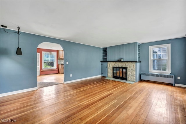 8743 Usher Rd, Olmsted Twp, OH 44138 - unfurnished living room with radiator heating unit, light wood-type flooring, arched walkways, and a fireplace