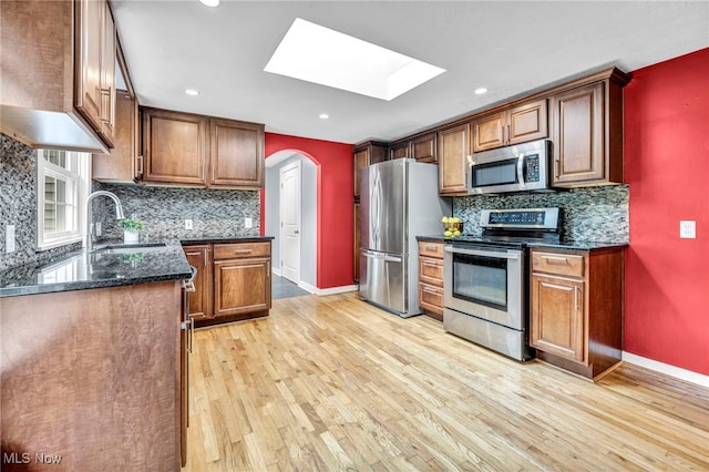 8743 Usher Rd, Olmsted Twp, OH 44138 - kitchen with stainless steel appliances, arched walkways, a skylight, light wood finished floors, and tasteful backsplash
