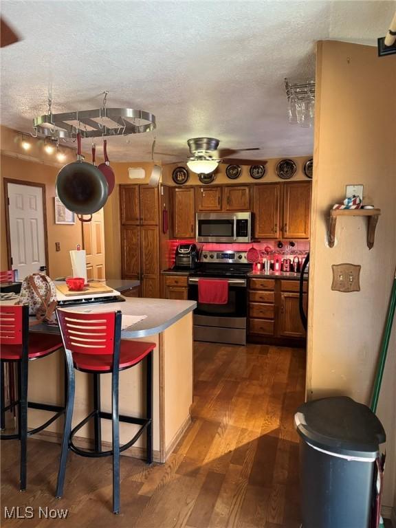 20684 Albion Rd, Strongsville, OH 44149 - kitchen featuring stainless steel appliances, brown cabinets, a textured ceiling, wood finished floors, and a kitchen bar