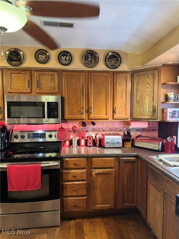 20684 Albion Rd, Strongsville, OH 44149 - kitchen featuring stainless steel appliances, decorative backsplash, brown cabinetry, wood finished floors, and dark countertops