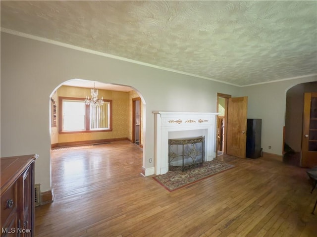 2323 Scholl Rd, University Heights, OH 44118 - unfurnished living room featuring arched walkways, wood-type flooring, a textured ceiling, a chandelier, and ornamental molding