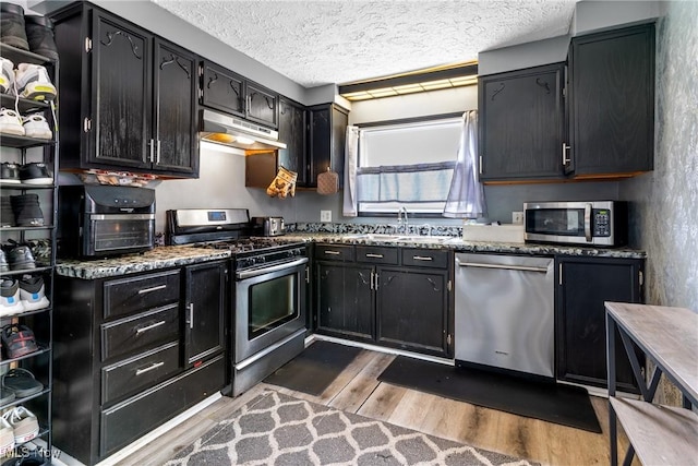 120 Palmetto Ave, Bedford, OH 44146 - kitchen featuring appliances with stainless steel finishes, under cabinet range hood, dark cabinets, wood finished floors, and a textured ceiling