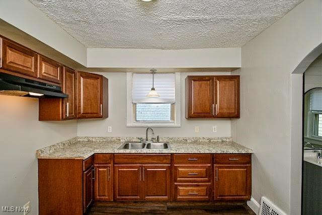 608 Columbus Ave NW, Canton, OH 44708 - kitchen featuring under cabinet range hood, a textured ceiling, dark wood finished floors, arched walkways, and brown cabinetry