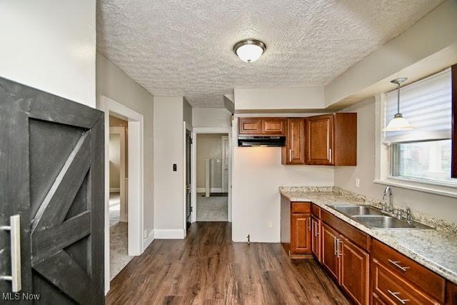 608 Columbus Ave NW, Canton, OH 44708 - kitchen with dark wood-type flooring, a textured ceiling, brown cabinets, pendant lighting, and under cabinet range hood