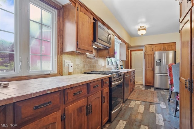 3571 Greenwich Rd, Barberton, OH 44203 - kitchen featuring stainless steel appliances, dark wood-style floors, backsplash, tile counters, and brown cabinetry