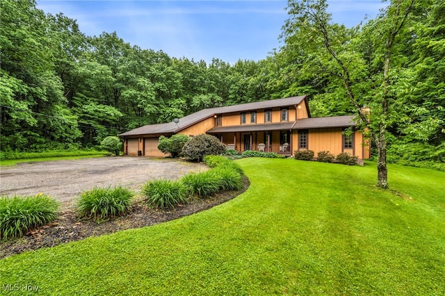 12938 Carter Rd, Leroy, OH 44077 - view of front facade featuring a porch, gravel driveway, an attached garage, a front lawn, and a forest view
