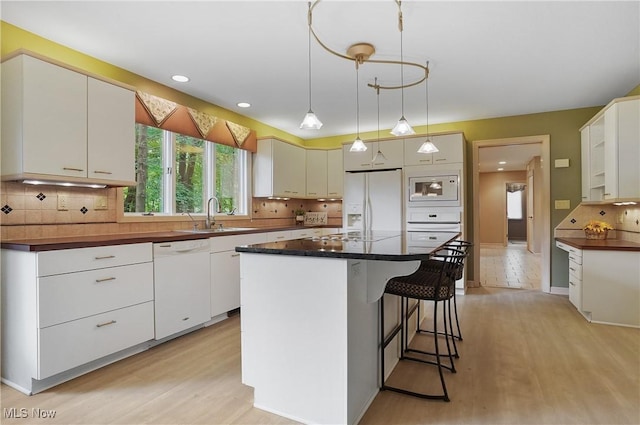 80 Hawthorne Ave, Rittman, OH 44270 - kitchen featuring white appliances, light wood-style floors, dark countertops, a kitchen island, and decorative backsplash