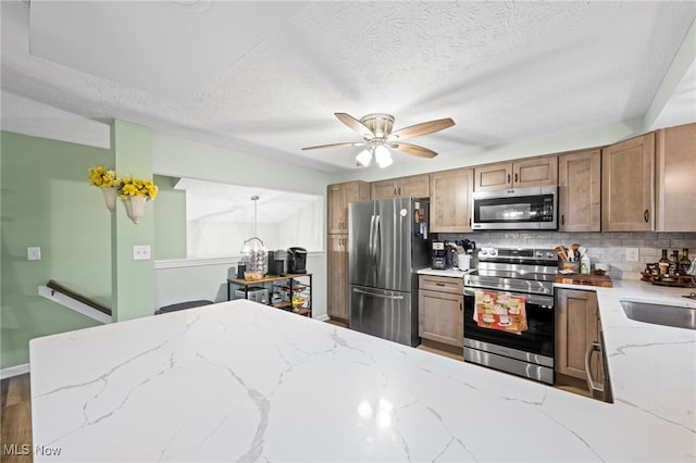 7152 Rippling Brook Ln, Concord, OH 44060 - kitchen featuring appliances with stainless steel finishes, tasteful backsplash, a ceiling fan, light stone counters, and brown cabinetry