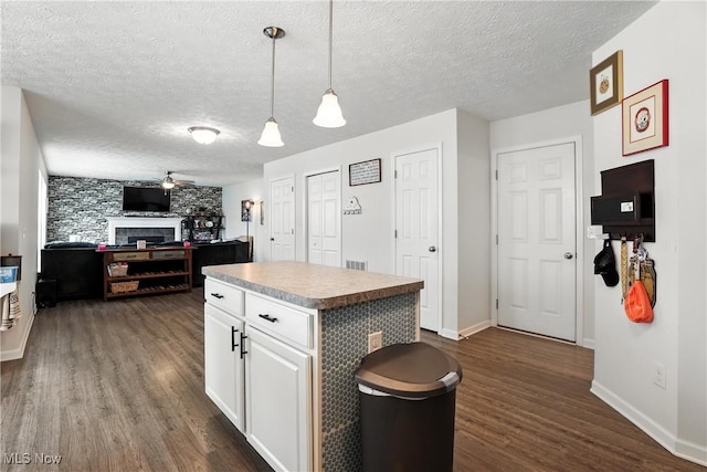 3990 Abigail Dr, Lorain, OH 44053 - kitchen with dark wood-style flooring, a textured ceiling, a fireplace, white cabinetry, and a kitchen island