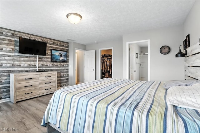 3990 Abigail Dr, Lorain, OH 44053 - bedroom featuring light wood-style flooring, a spacious closet, a textured ceiling, wooden walls, and ensuite bath