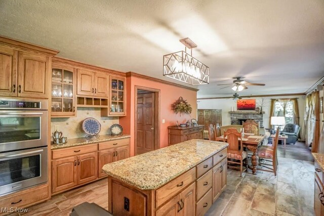3020 Crookston Ln, Clinton, OH 44216 - kitchen with double oven, a ceiling fan, a fireplace, light stone countertops, and glass insert cabinets