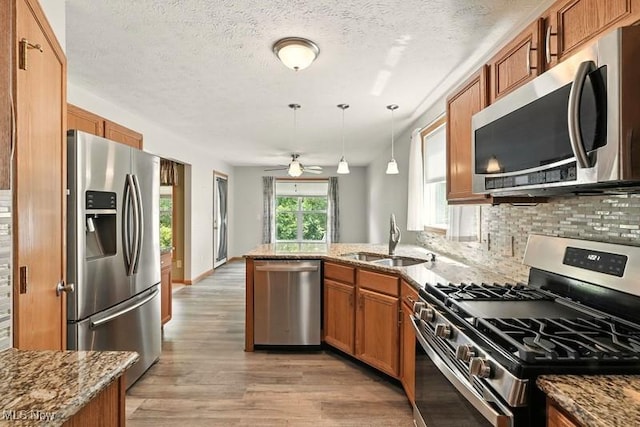 1367 Hidden Lake Blvd, Akron, OH 44312 - kitchen featuring stainless steel appliances, brown cabinetry, light wood finished floors, dark stone counters, and backsplash