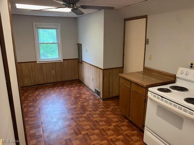 1543 Genesee Rd, South Euclid, OH 44121 - kitchen with white range with electric stovetop, wainscoting, wooden walls, ceiling fan, and brown cabinets