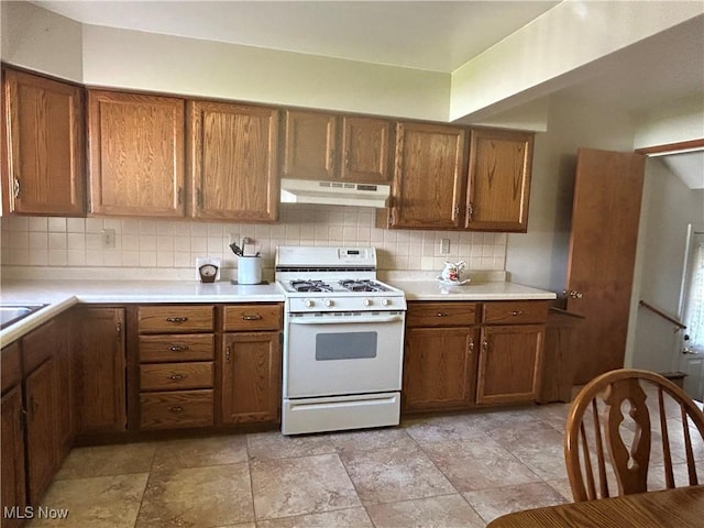 145 Marcia Dr, Austintown, OH 44515 - kitchen with white gas range oven, under cabinet range hood, backsplash, brown cabinetry, and light countertops