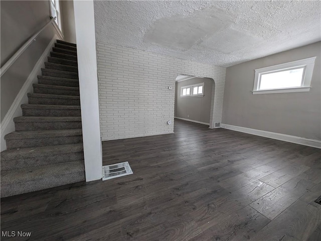 3947 W 22nd St, Cleveland, OH 44109 - unfurnished living room featuring brick wall, a textured ceiling, stairway, dark wood-style flooring, and arched walkways