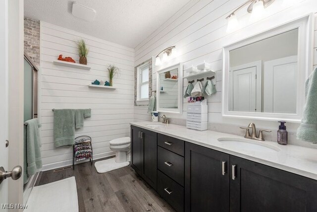 12187 Bexley Dr, Grafton, OH 44044 - full bathroom with double vanity, wood walls, wood finished floors, an enclosed shower, and a textured ceiling