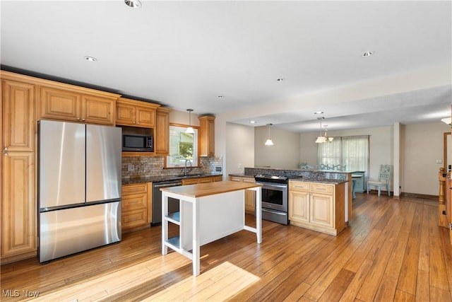 7298 Stonehill Ave NW, Canal Fulton, OH 44614 - kitchen with appliances with stainless steel finishes, a peninsula, decorative backsplash, light wood finished floors, and hanging light fixtures