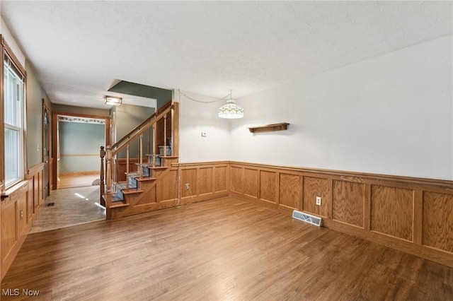 3594 Heckman St NW, Uniontown, OH 44685 - empty room featuring a wainscoted wall, light wood-type flooring, stairway, and a textured ceiling
