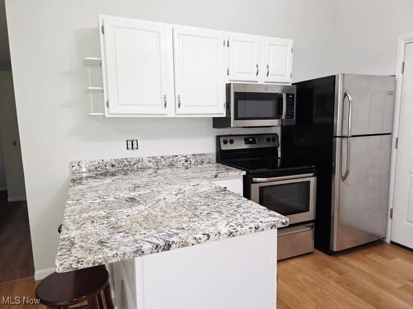 7957 Pamela Dr, North Royalton, OH 44133 - kitchen featuring stainless steel appliances, a peninsula, white cabinetry, and light wood-type flooring
