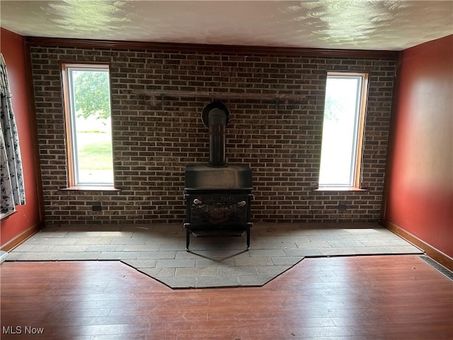 14260 Canaan Center Rd, Creston, OH 44217 - unfurnished living room featuring a wood stove, wood-type flooring, healthy amount of natural light, and brick wall
