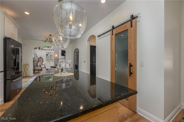 3595 Vineyard Ave NW, Canton, OH 44708 - kitchen with black refrigerator with ice dispenser, arched walkways, a barn door, light wood-style floors, and dark stone counters