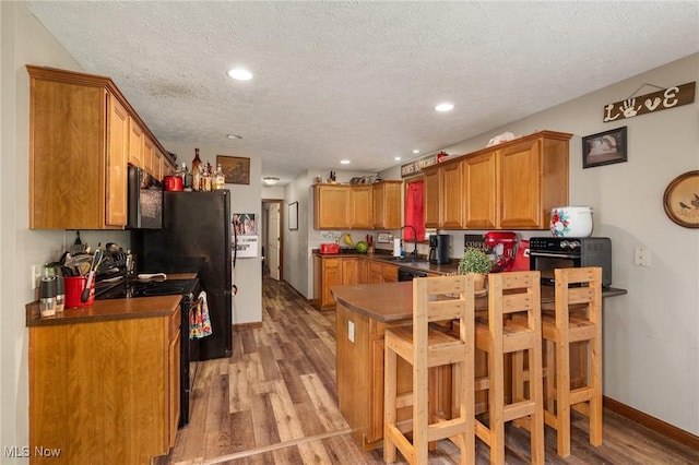 1345 County Road 16, New London, OH 44851 - kitchen featuring black range with gas cooktop, a peninsula, light wood-style floors, dark countertops, and brown cabinets