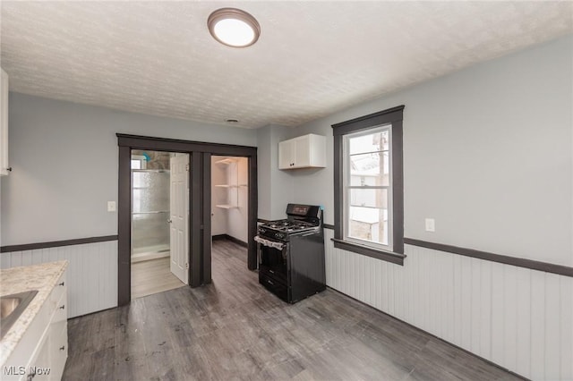 1431 Rowley Ave, Cleveland, OH 44109 - kitchen featuring black range with gas cooktop, a wainscoted wall, white cabinetry, wood finished floors, and light countertops