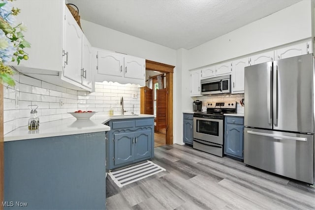 201 E Spring St, Marietta, OH 45750 - kitchen featuring appliances with stainless steel finishes, blue cabinets, tasteful backsplash, light wood finished floors, and light countertops