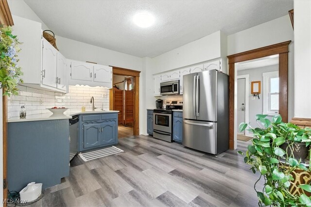 201 E Spring St, Marietta, OH 45750 - kitchen featuring stainless steel appliances, white cabinetry, tasteful backsplash, light wood-type flooring, and a textured ceiling