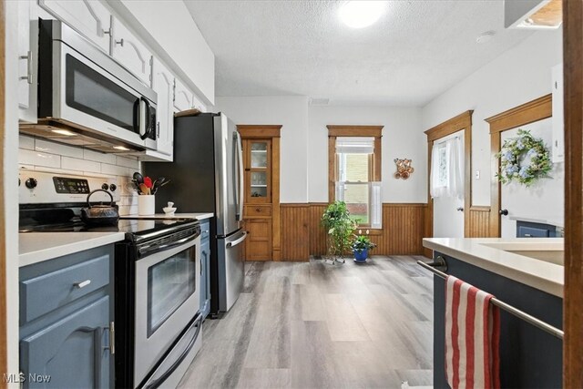 201 E Spring St, Marietta, OH 45750 - kitchen featuring stainless steel appliances, wainscoting, light wood-style floors, a textured ceiling, and wood walls