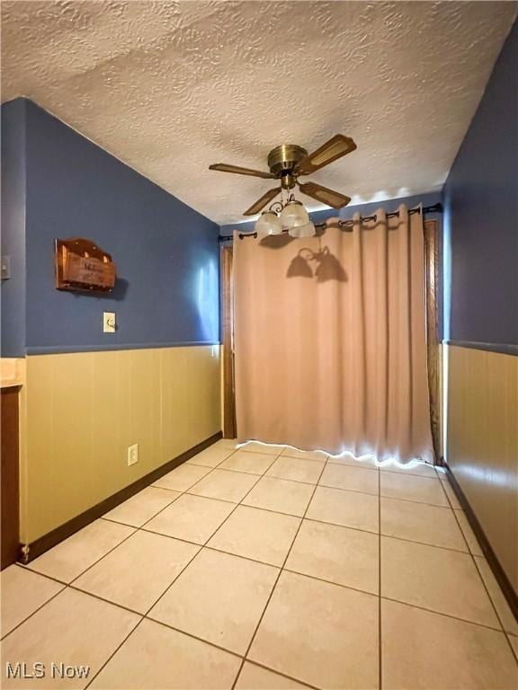 1422 Youll St, Niles, OH 44446 - empty room featuring a ceiling fan, a wainscoted wall, a textured ceiling, and light tile patterned floors