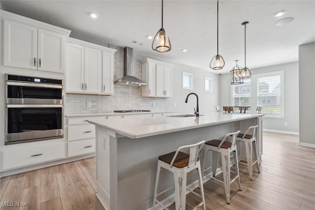 23761 St Andrews Dr, Columbia Station, OH 44028 - kitchen featuring wall chimney exhaust hood, stainless steel double oven, light wood-type flooring, an island with sink, and white cabinets