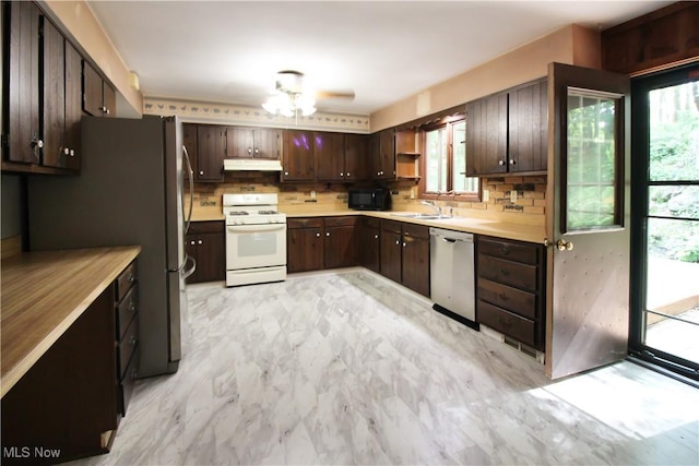 8630 Williams Rd, Chardon, OH 44024 - kitchen with stainless steel appliances, under cabinet range hood, light marble finish floors, dark brown cabinetry, and decorative backsplash