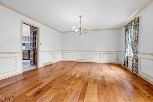 8640 Foxglove Ave NW, Clinton, OH 44216 - unfurnished room with a chandelier, light wood-type flooring, ornamental molding, a decorative wall, and wainscoting