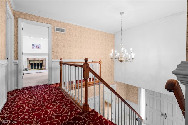 8640 Foxglove Ave NW, Clinton, OH 44216 - staircase featuring wallpapered walls, a chandelier, crown molding, a brick fireplace, and carpet flooring