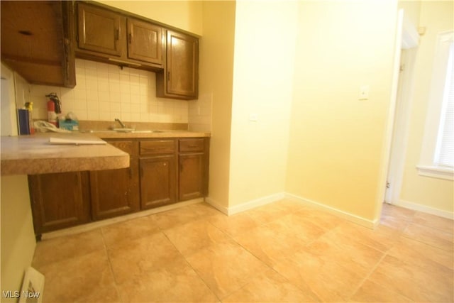 853 E 144th St, Cleveland, OH 44110 - kitchen featuring tasteful backsplash, light countertops, brown cabinetry, and light tile patterned floors
