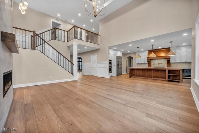 2705 Rocky Ridge Dr, Westlake, OH 44145 - unfurnished living room featuring light wood-style flooring, a chandelier, a high ceiling, a fireplace, and stairway